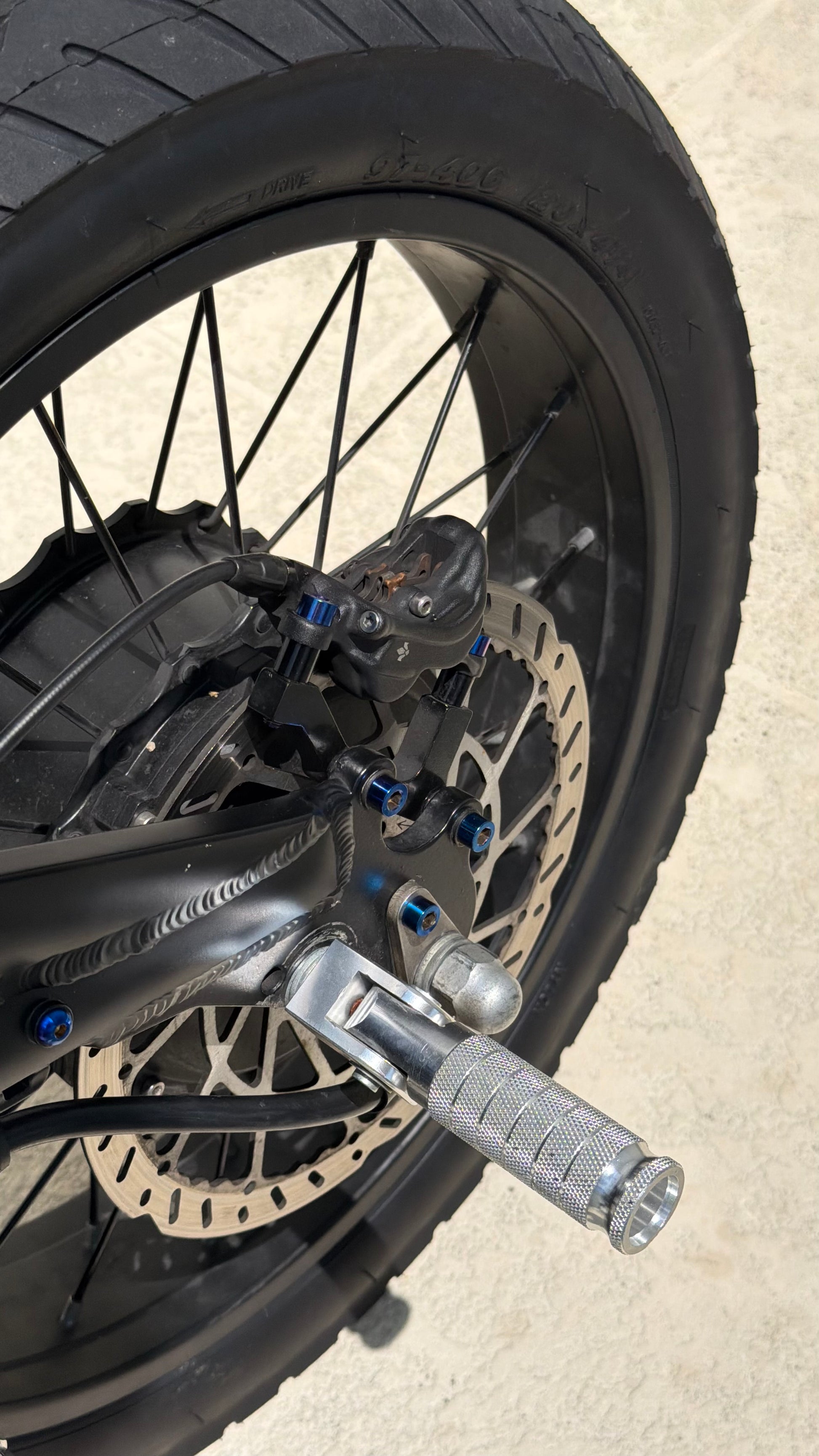 Close-up of a motorcycle wheel with disc brake and foot peg on a concrete surface