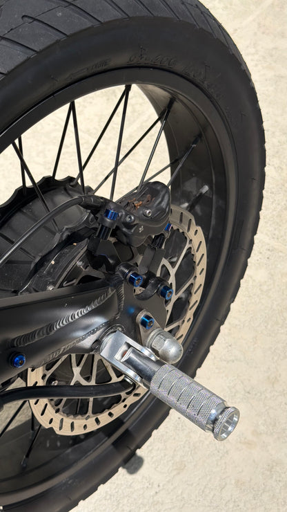 Close-up of a motorcycle wheel with disc brake and foot peg on a concrete surface