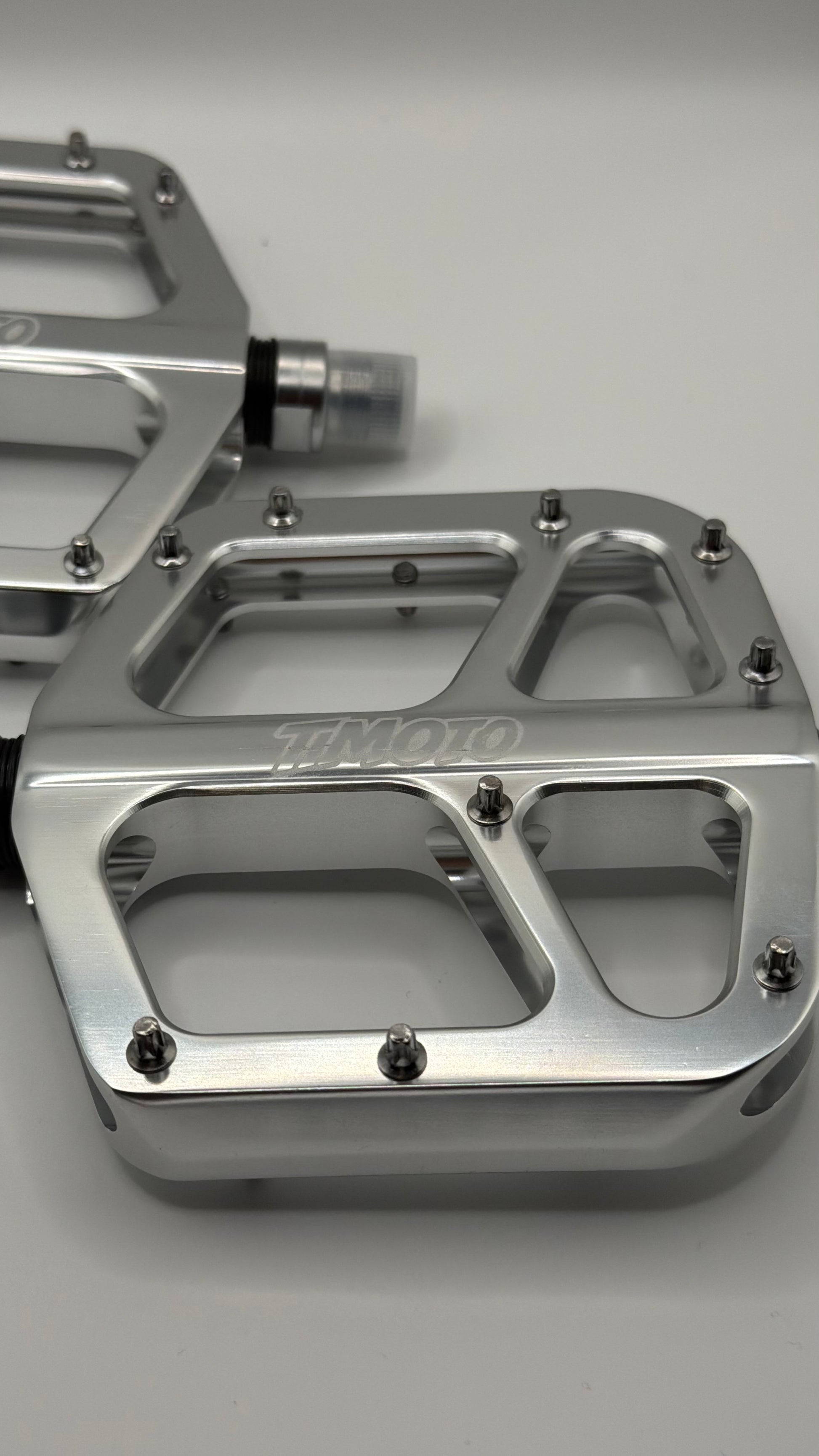 Metallic foot pegs with 'timoto' branding on a gray background