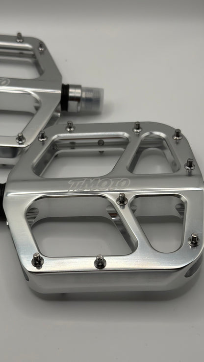 Metallic foot pegs with 'timoto' branding on a gray background